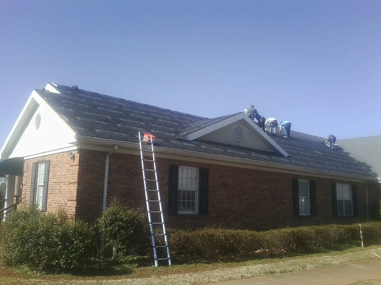 Crew tearing shingles off a brick ranch roof with a ladder set — Metal Roof Repair work by our crew in Lehigh
