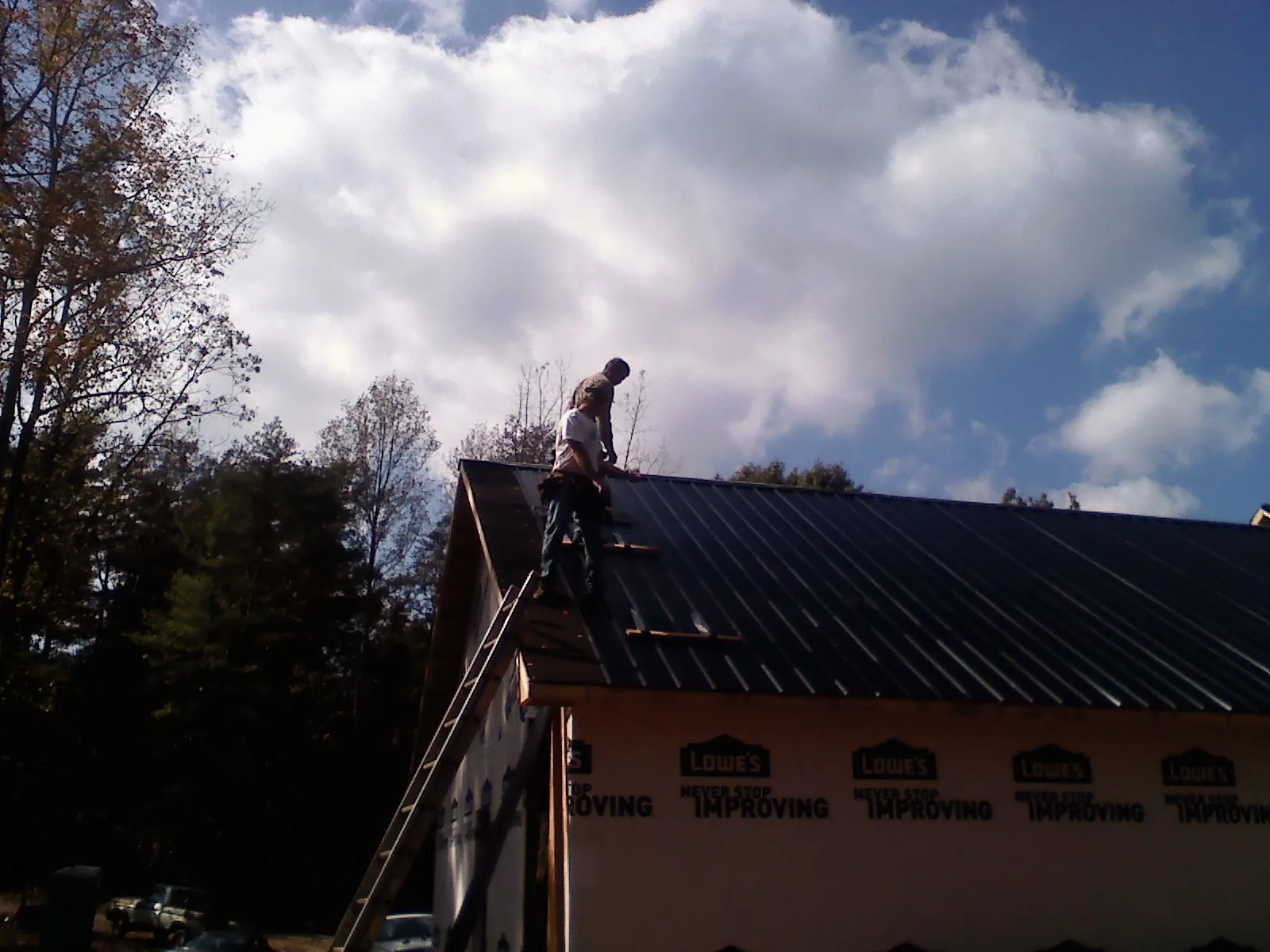 Roofer fastening dark metal panels high against a cloudy sky, from a Roof Inspection job in Lehigh